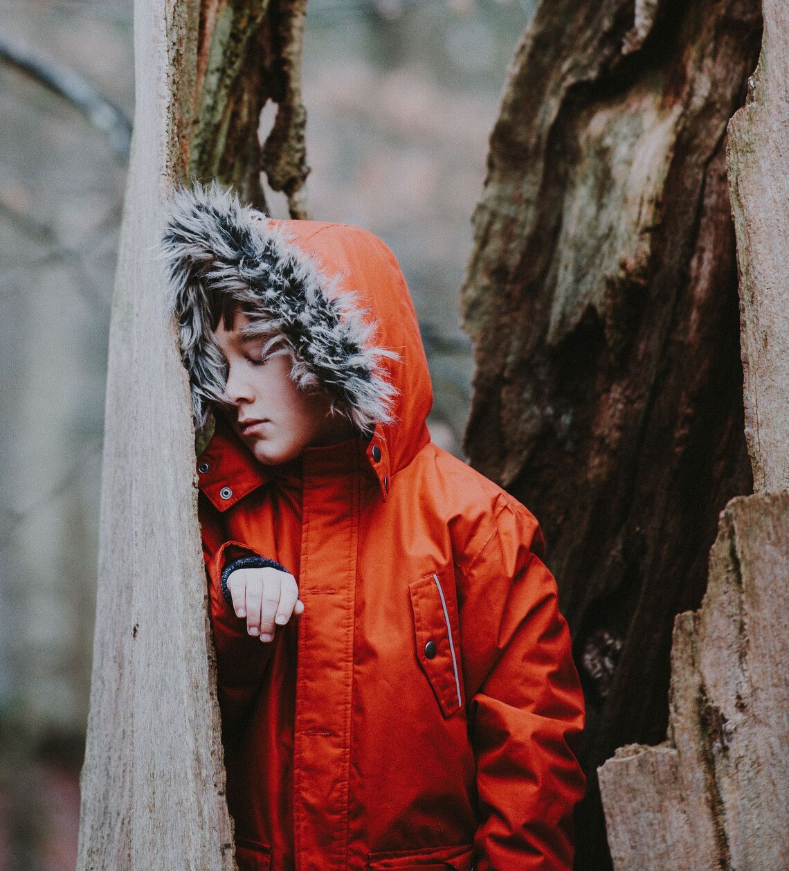 A boy leaning against a tree with his eyes closed 